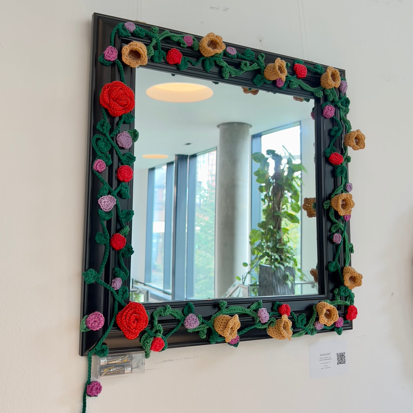 Unique square black mirror frame adorned with handmade 3D crochet roses and vines in red, orange, and purple, available at HEADS Art Gallery.