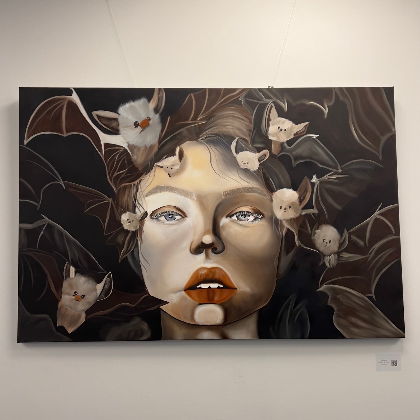 Painting of a woman's face surrounded by numerous small, fluffy white bats against a dark background, available at HEADS Art Gallery.
