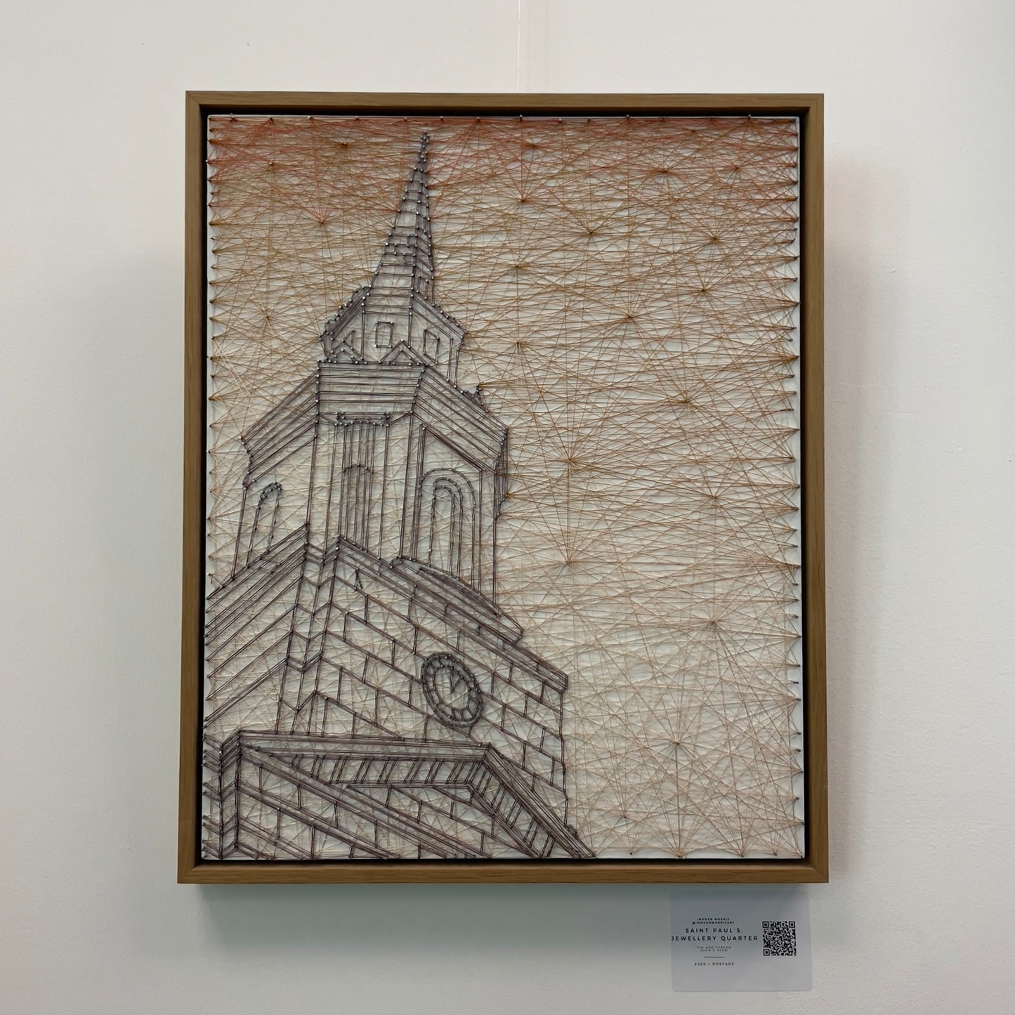 String art piece depicting a grand clock tower spire against a sunset-toned geometric background, housed in a natural wood frame, available at HEADS Art Gallery.
