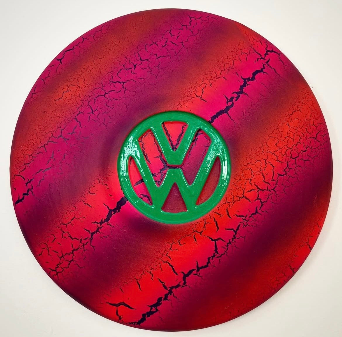 A painted metal hub cap with a red background and black and green volkswagen emblem in the center.