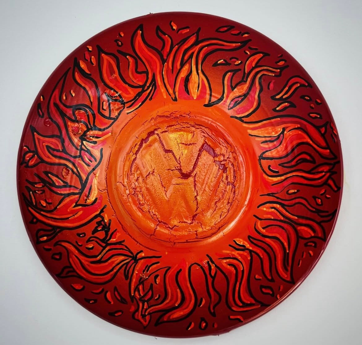 A painted metal hub cap with a volkswagen logo in the center, surrounded by a red and black fire paint design.