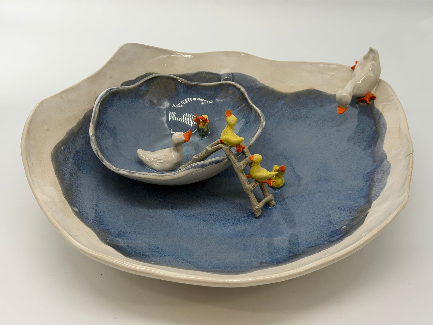 Ceramic dish with blue interior and white exterior, featuring small ceramic ducks on a ladder.
