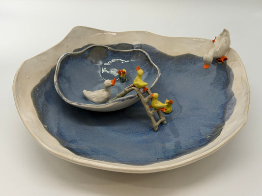 Ceramic dish with blue interior and white exterior, featuring small ceramic ducks on a ladder.