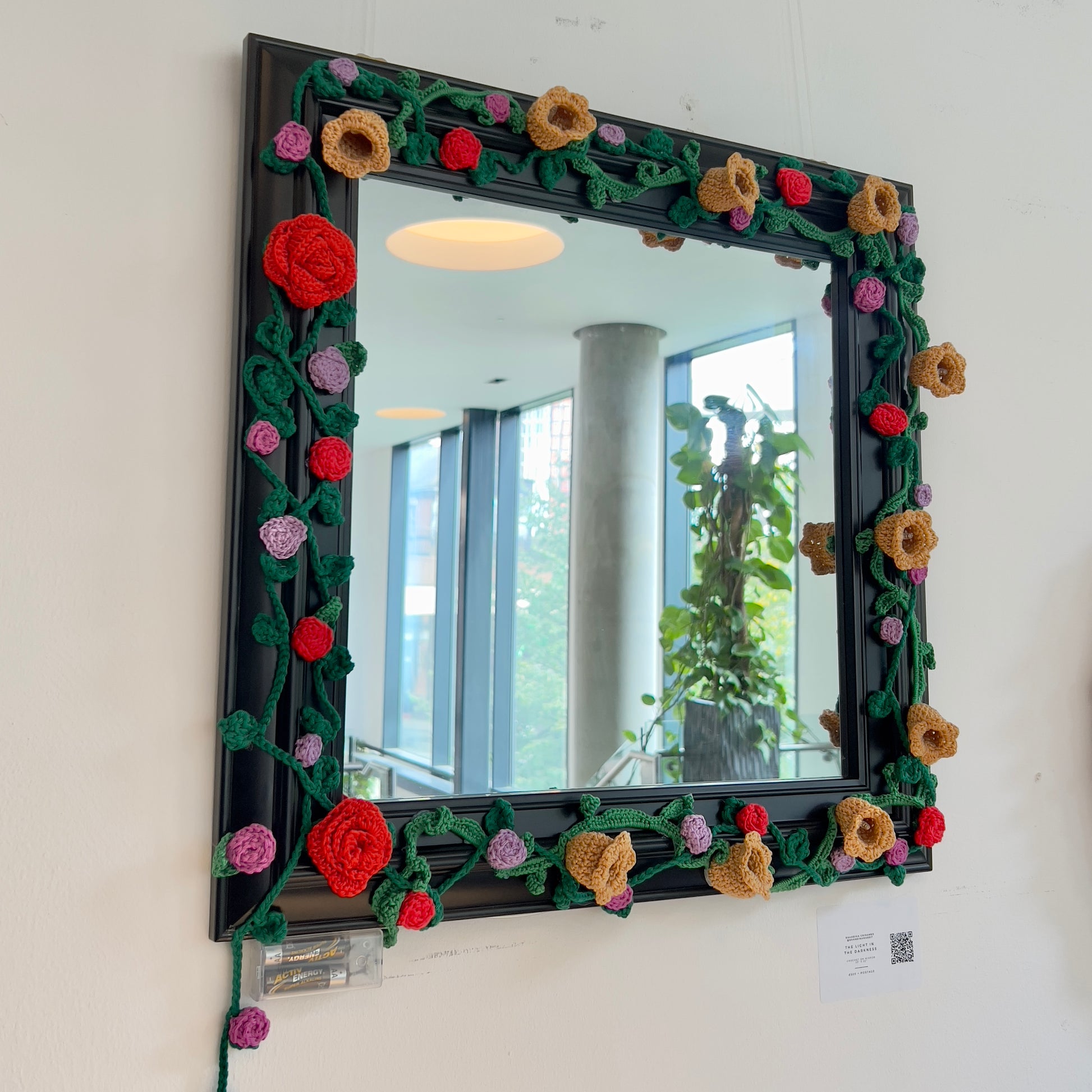 Unique square black mirror frame adorned with handmade 3D crochet roses and vines in red, orange, and purple, available at HEADS Art Gallery.