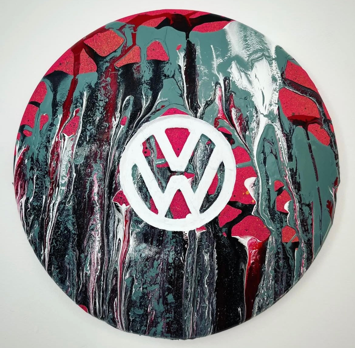 A painted metal hub cap with a volkswagen logo in the center, surrounded by a swirl of red and black paint.