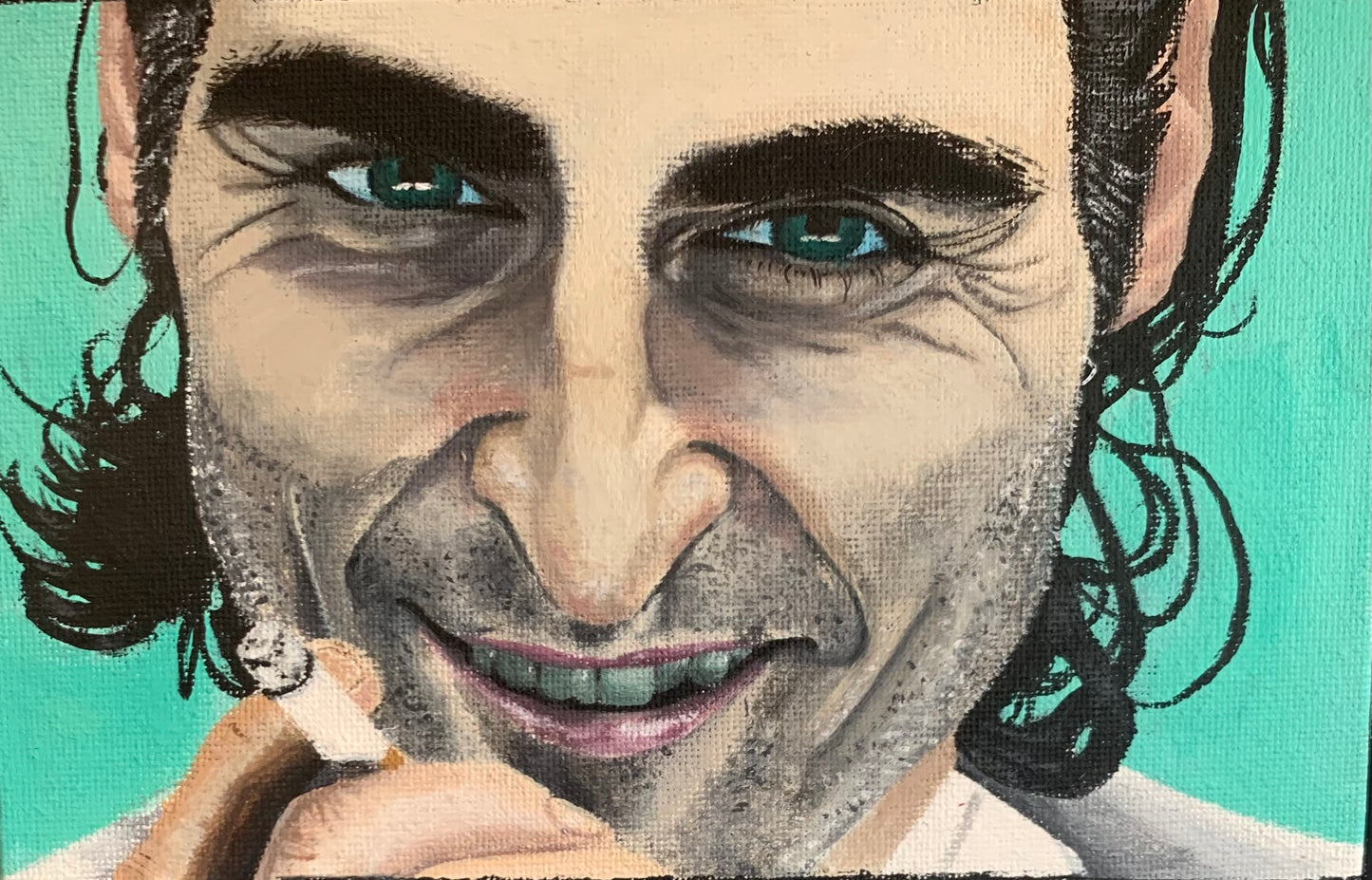 Portrait of Joaquin Phoenix as the Joker with a slight smile, holding a cigarette against a bright teal background, available at HEADS Art Gallery.