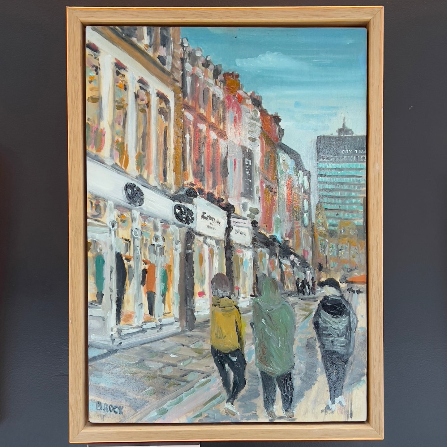 A vibrant street-level painting of Manchester featuring figures walking past storefronts with the City Tower visible in the distance, available at HEADS Art Gallery.