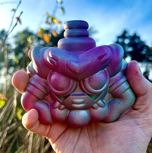 Stylized character face with a metallic iridescent purple and blue finish, available at HEADS Art Gallery.