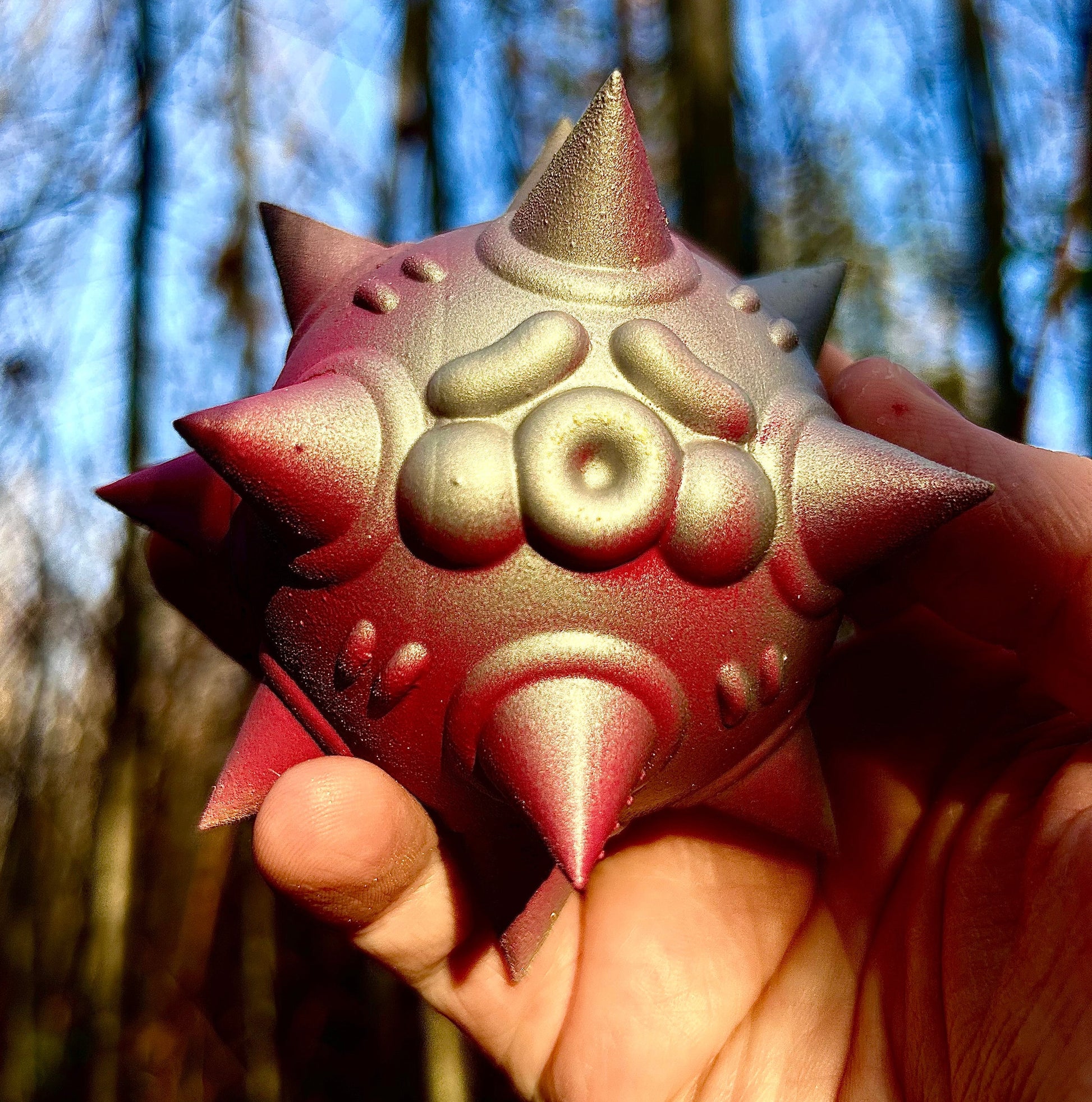 Spiked geometric sculpture with a metallic iridescent gold and red finish, available at HEADS Art Gallery.