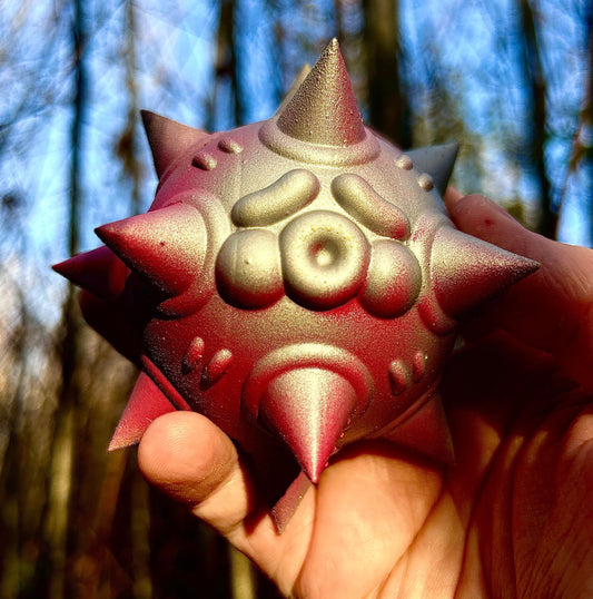 Spiked geometric sculpture with a metallic iridescent gold and red finish, available at HEADS Art Gallery.