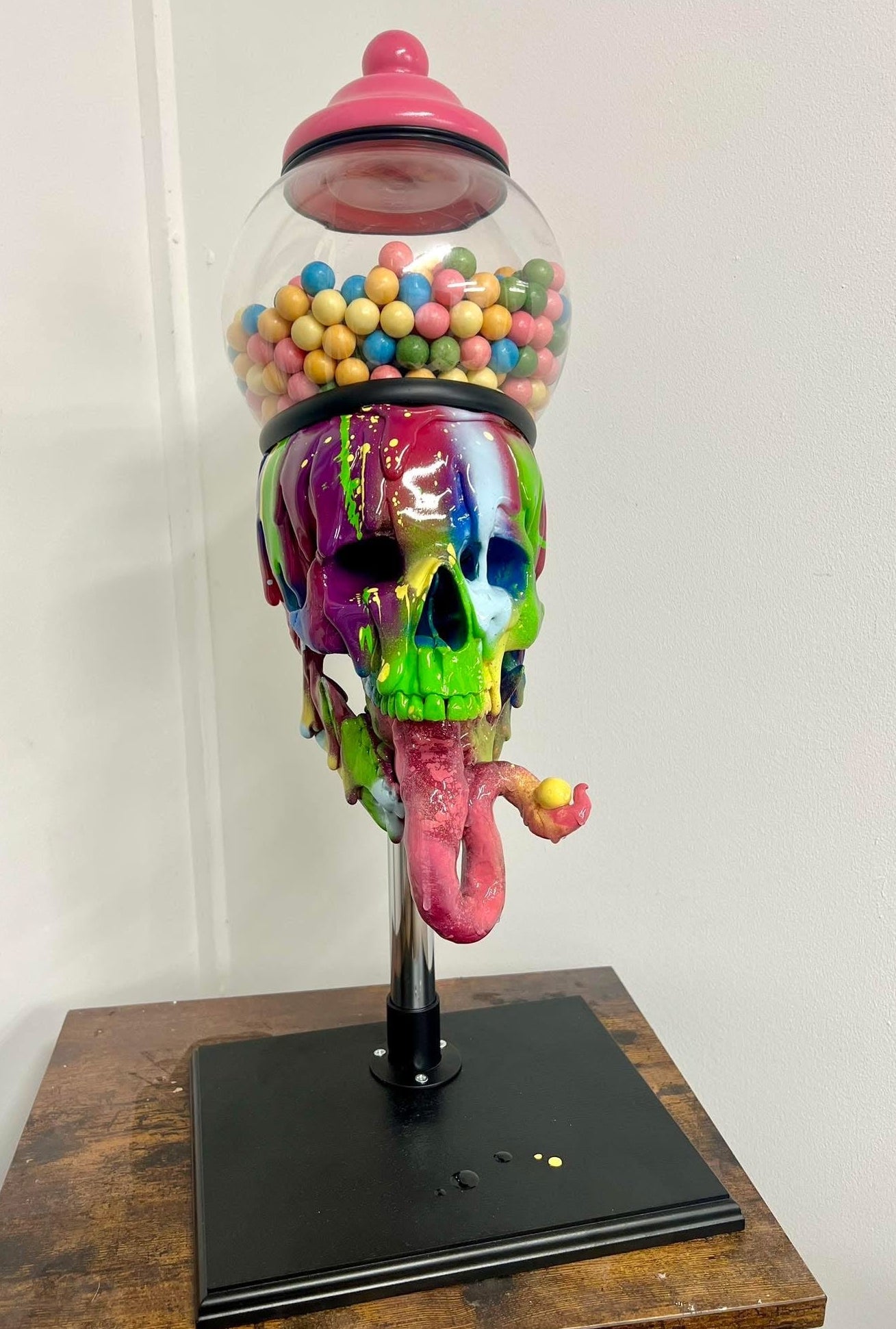 Colorful melting rainbow skull glass gumball machine filled with colourful candy sculpture on a wooden base available at HEADS Art Gallery.