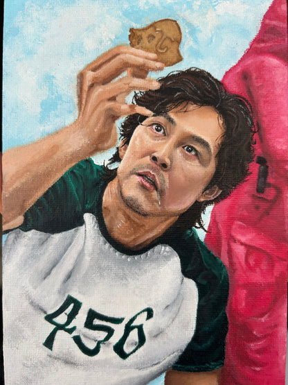 Realistic portrait painting of Lee Jung-jae as Seong Gi-hun from Squid Game, focusing on his player number 456 and the dalgona honeycomb challenge, available at HEADS Art Gallery.